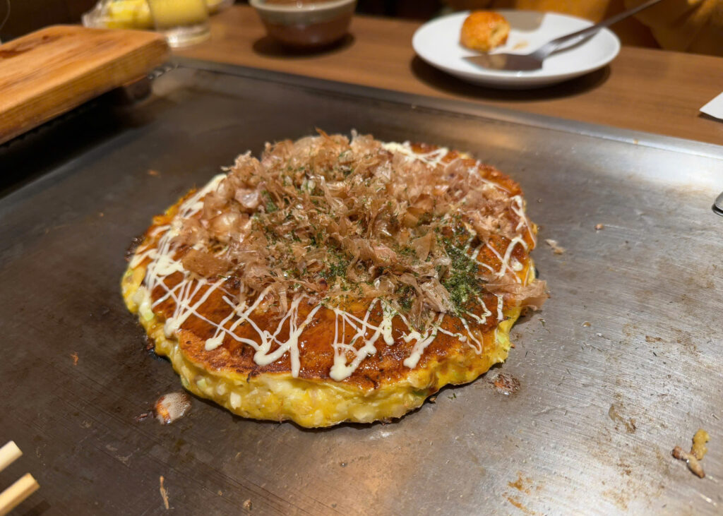 Freshly cooked okonomiyaki topped with bonito flakes and okonomiyaki sauce on a teppan grill